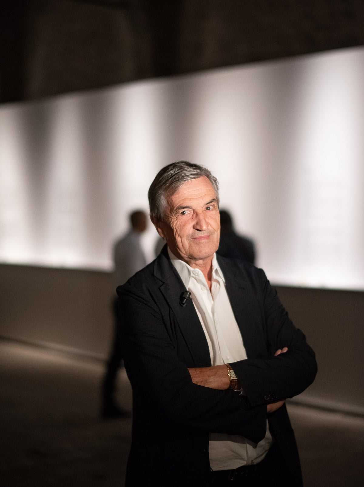 Portret van parfumeur en auteur Jean-Claude Ellena in een donker jasje en wit overhemd, met bomen op de achtergrond.