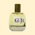 A studio product photograph of a clear glass perfume bottle filled with pale yellow-green fragrance, topped with a reflective gold cylindrical cap and set against a soft cream background. A white label on the front displays the Collection Trente-Cinq logo and the name “Flavia Romana Durante.” The transparent bottle reveals the light-colored perfume, while soft reflections on the glass emphasize its rounded, sculptural shape.