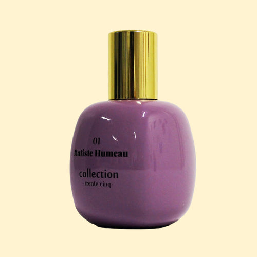 A studio product photograph of a rounded lavender-purple perfume bottle with a reflective gold cylindrical cap, set against a soft cream background. Black text on the bottle reads “01 Batiste Humeau” and “collection ·trente cinq·”. The bottle has a glossy finish with subtle reflections highlighting its curved shape.