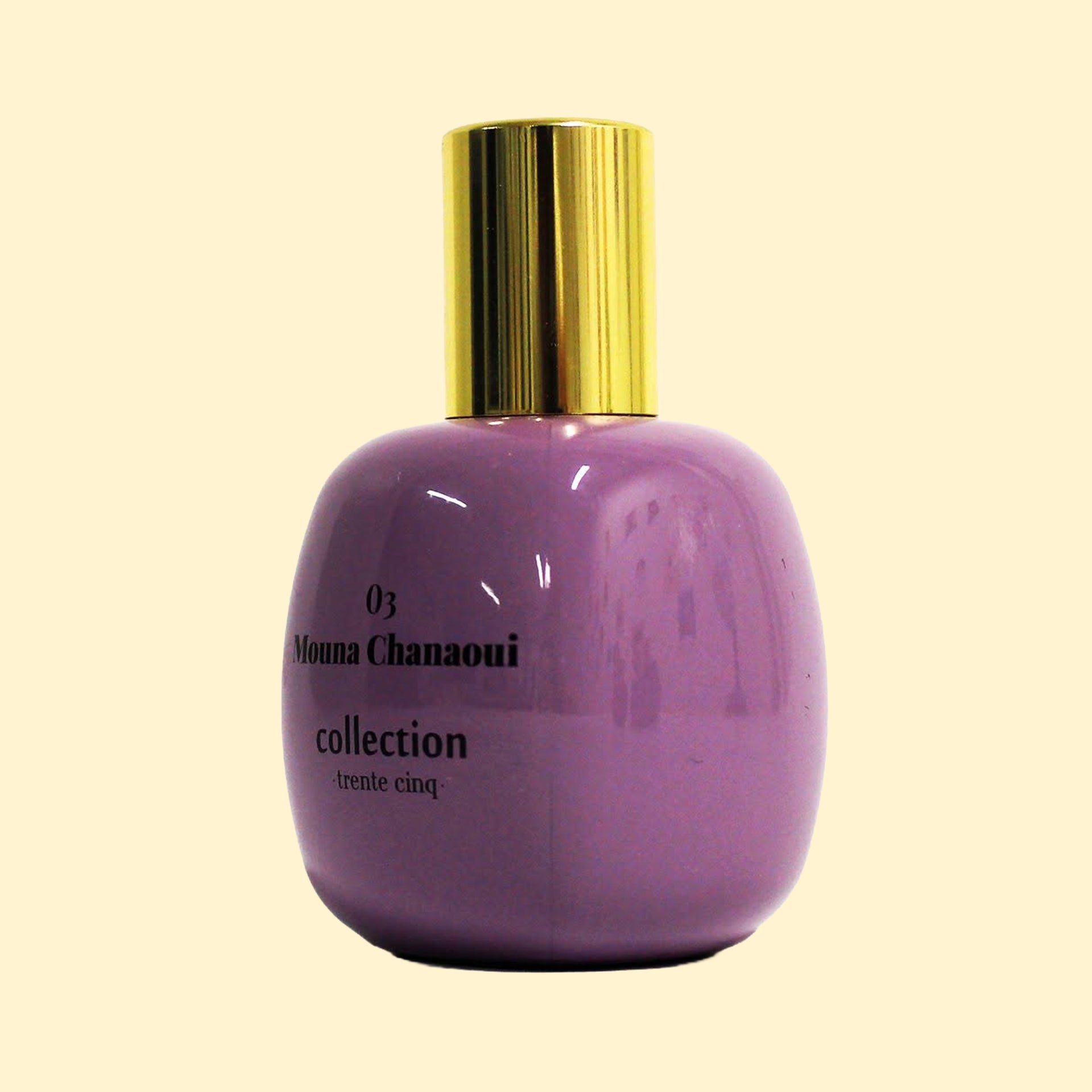 A studio product photograph of a rounded lavender-purple perfume bottle with a reflective gold cylindrical cap, set against a soft cream background. Black text on the bottle reads “03 Mouna Chanaoui” and “collection ·trente cinq·”. The bottle’s glossy finish catches soft reflections, highlighting its smooth, rounded silhouette.