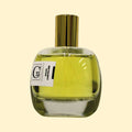 A studio product photograph of a clear glass perfume bottle filled with yellow-green fragrance, topped with a reflective gold cylindrical cap and set against a soft cream background. A white label on the front displays the Collection Trente-Cinq logo and the name “Maud Chevalier.” The transparent bottle reveals the luminous color of the perfume, while soft reflections on the glass emphasize its rounded, sculptural shape.