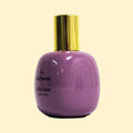 A studio product photograph of a rounded lavender-purple perfume bottle with a reflective gold cylindrical cap, set against a soft cream background. Black text on the bottle reads “05 Saif Parvez” and “collection ·trente cinq·”. The glossy finish and gentle reflections emphasise the bottle’s smooth, rounded contours.
