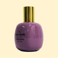 A studio product photograph of a rounded lavender-purple perfume bottle with a reflective gold cylindrical cap, set against a soft cream background. Black text on the bottle reads “02 Fanny Ginolin” and “collection ·trente cinq·”. The glossy bottle surface reflects the surrounding light, emphasising its smooth, sculptural form.