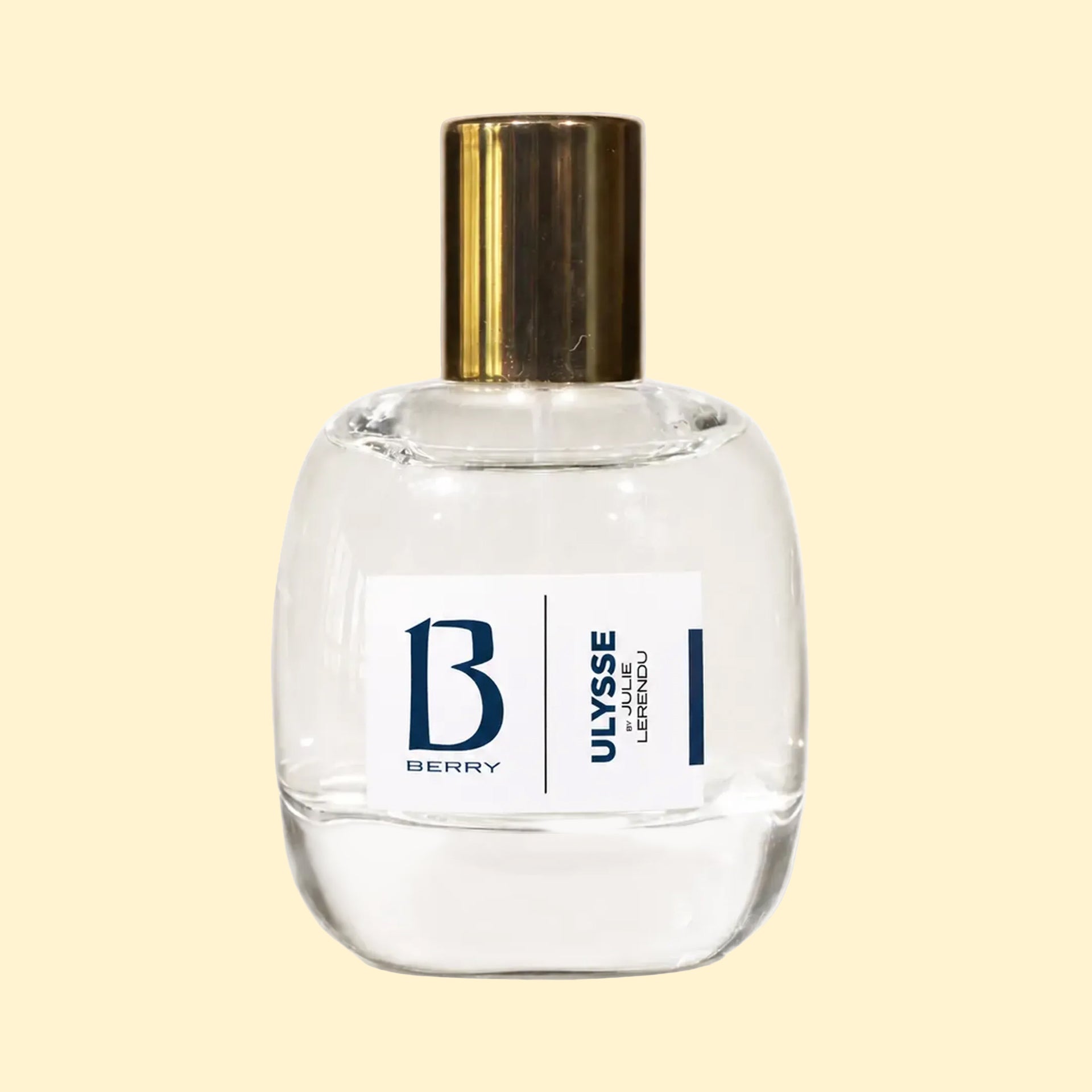 A studio product photograph of a clear glass perfume bottle filled with pale yellow-green fragrance, topped with a reflective gold cylindrical cap and set against a soft cream background. A white label on the front displays the Parfums Berry logo and the name “Julie Lerendu.” The transparent bottle highlights the soft hue of the perfume, while gentle reflections on the glass emphasise its rounded, sculptural silhouette.