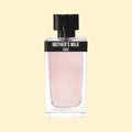 ERIS PARFUMS Mother’s Milk eau de parfum in a clear glass bottle with pale pink fragrance, black label and black cap, photographed against a soft cream background.