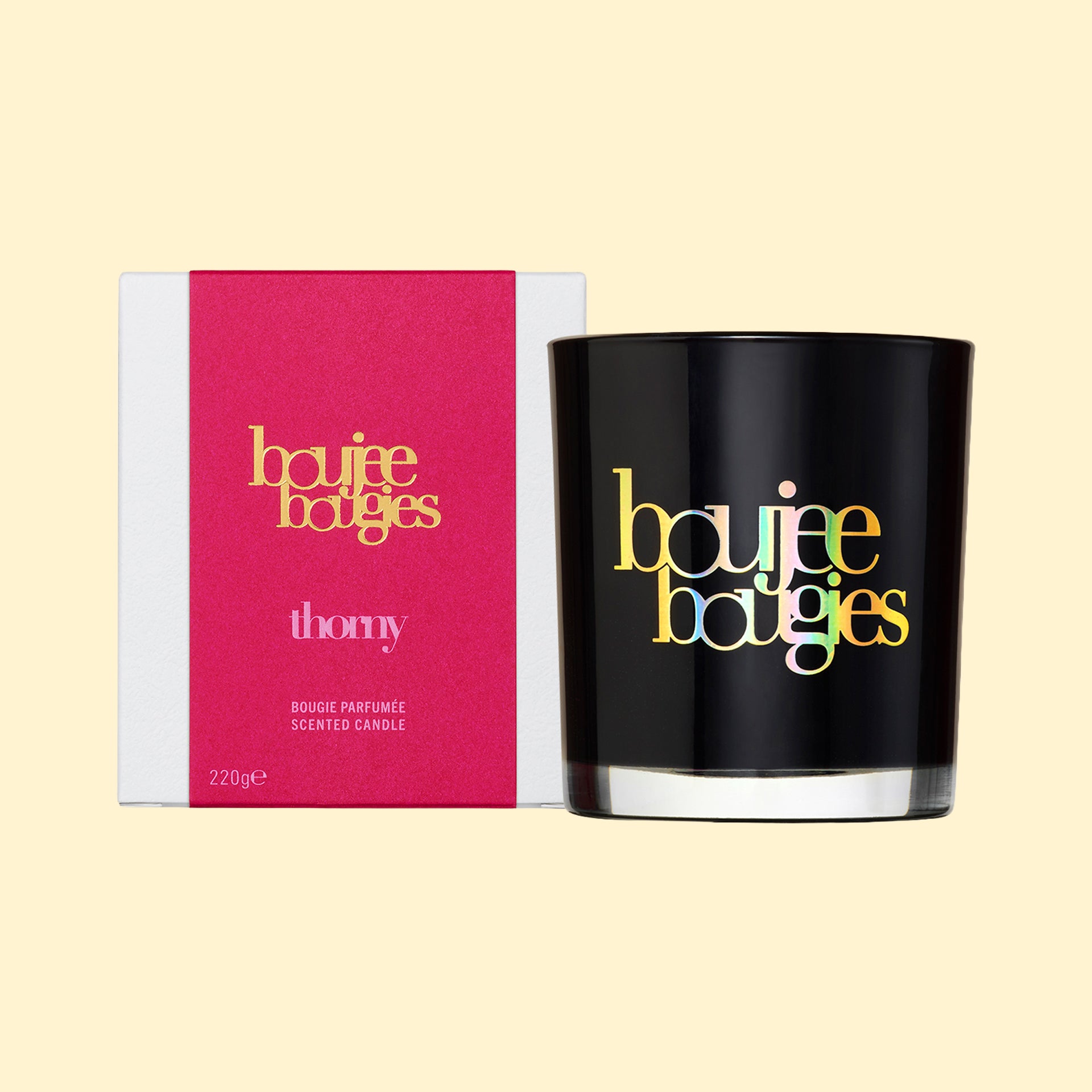 Boujee Bougies Thorny geurkaars van Olfiction in een glanzend zwart glazen glas naast de felroze en witte verpakking, 220g.