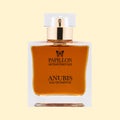 Papillon Artisan Perfumes Anubis Eau de Parfum in a clear rectangular glass bottle with a white cap and gold collar, filled with deep amber-brown fragrance against a soft cream background.
