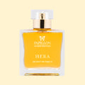 Papillon Artisan Perfumes Hera Extrait de Parfum in a clear rectangular glass bottle with a white cap and gold collar, featuring white lettering and filled with luminous golden fragrance against a soft cream background.