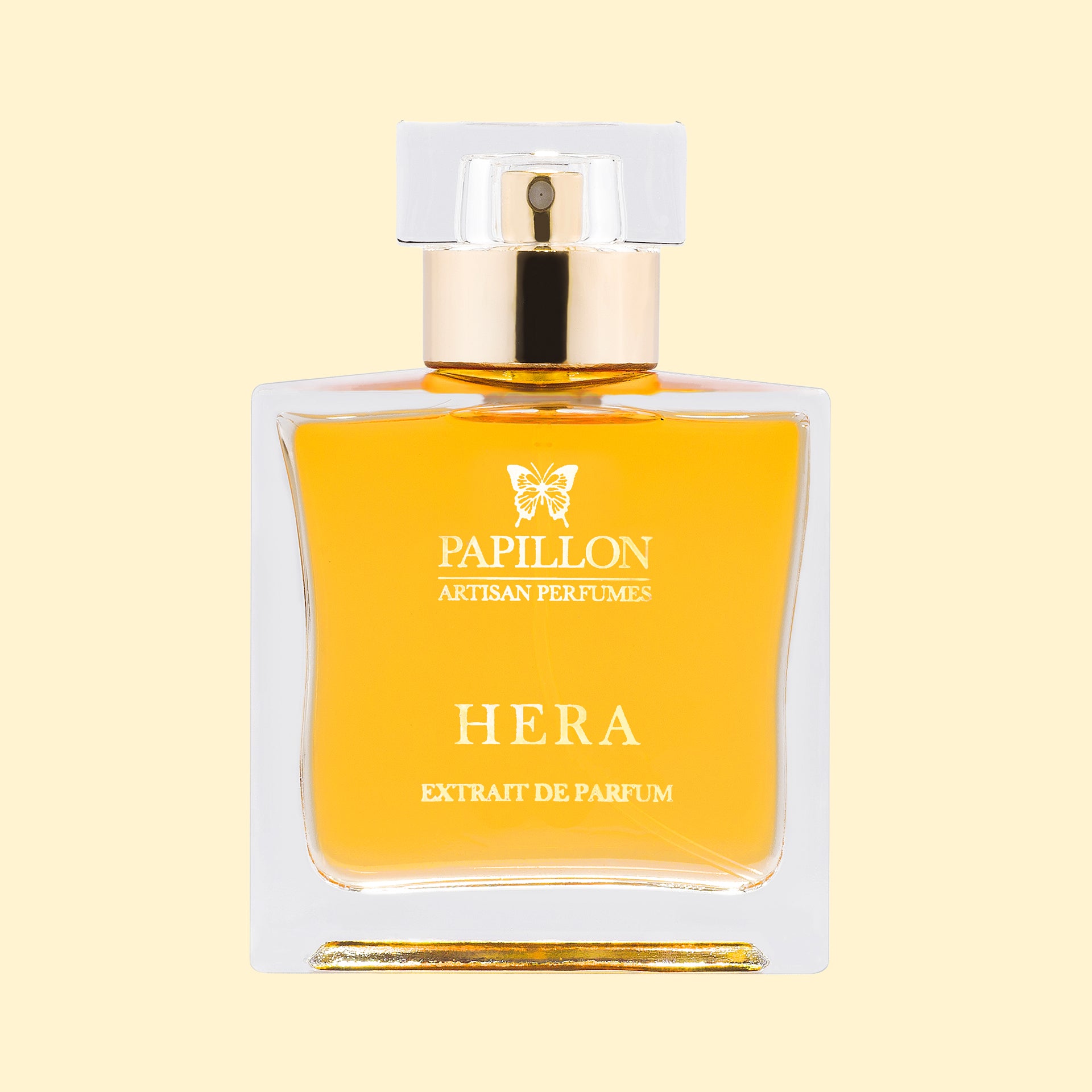Papillon Artisan Perfumes Hera Extrait de Parfum in a clear rectangular glass bottle with a white cap and gold collar, featuring white lettering and filled with luminous golden fragrance against a soft cream background.