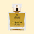 Papillon Artisan Perfumes Tobacco Rose Eau de Parfum in a clear rectangular glass bottle with a white cap and gold collar, filled with golden-honey coloured fragrance against a soft cream background.