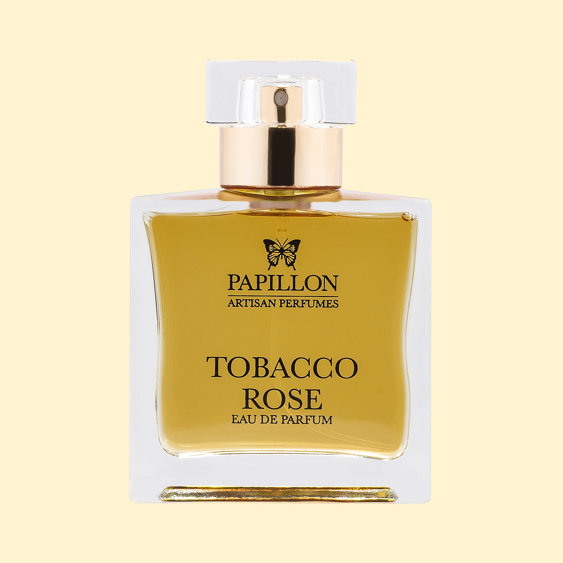 Papillon Artisan Perfumes Tobacco Rose Eau de Parfum in a clear rectangular glass bottle with a white cap and gold collar, filled with golden-honey coloured fragrance against a soft cream background.